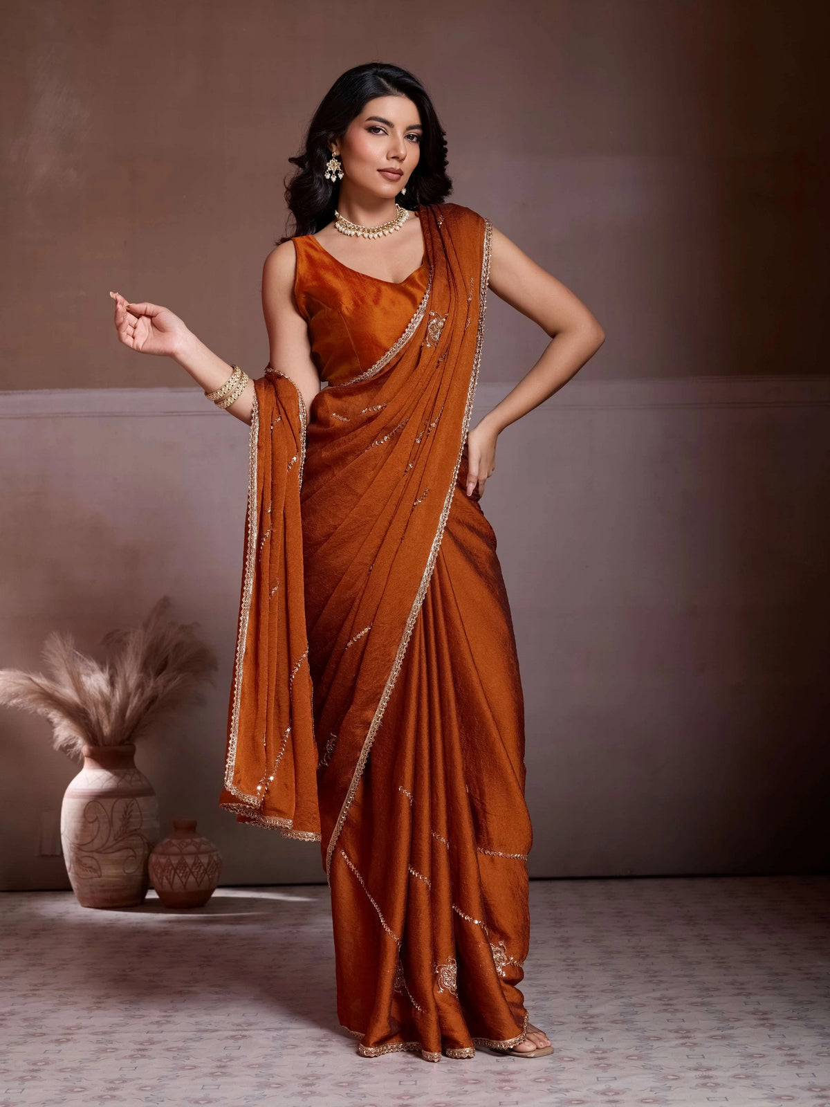 Woman in a traditional orange saree with gold border against a neutral background