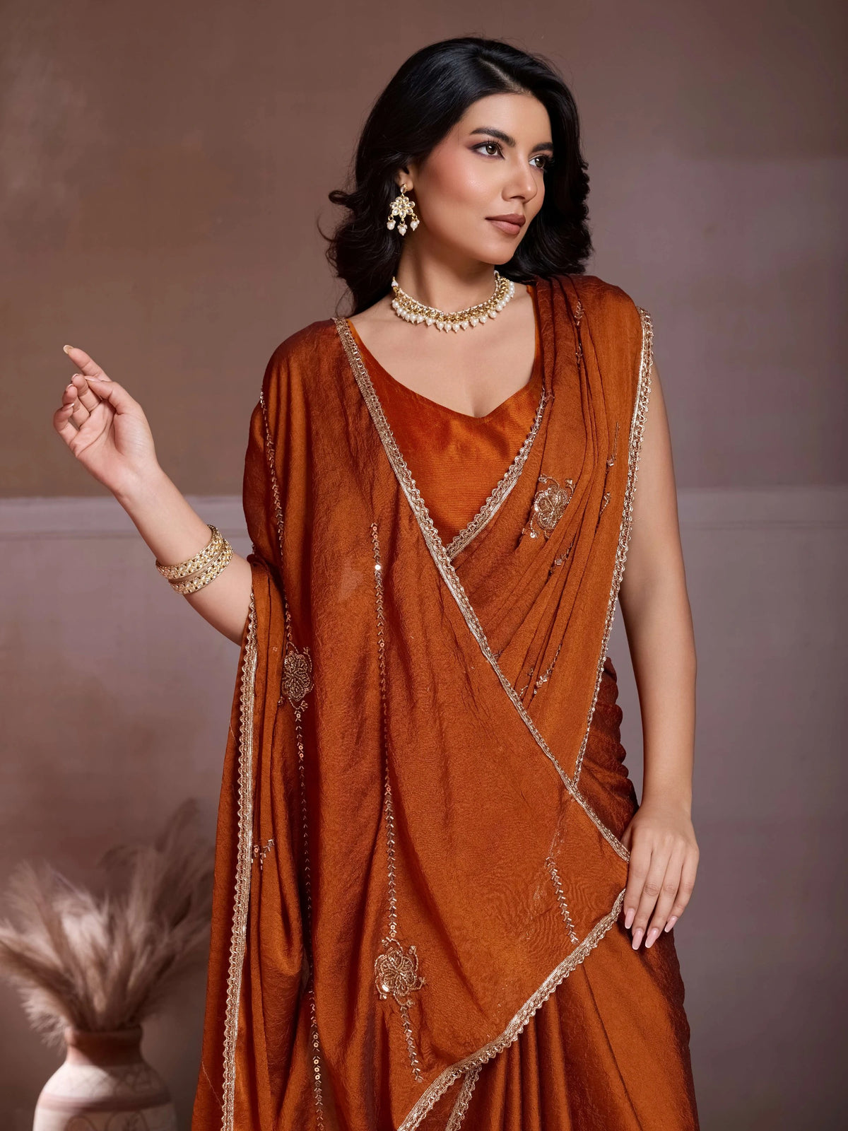 Woman wearing a rust-colored saree with gold embroidery against a neutral background