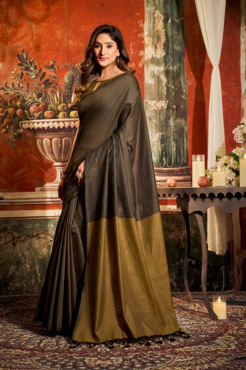 Woman in a dark green and brown saree standing in an ornate room with decorative elements.