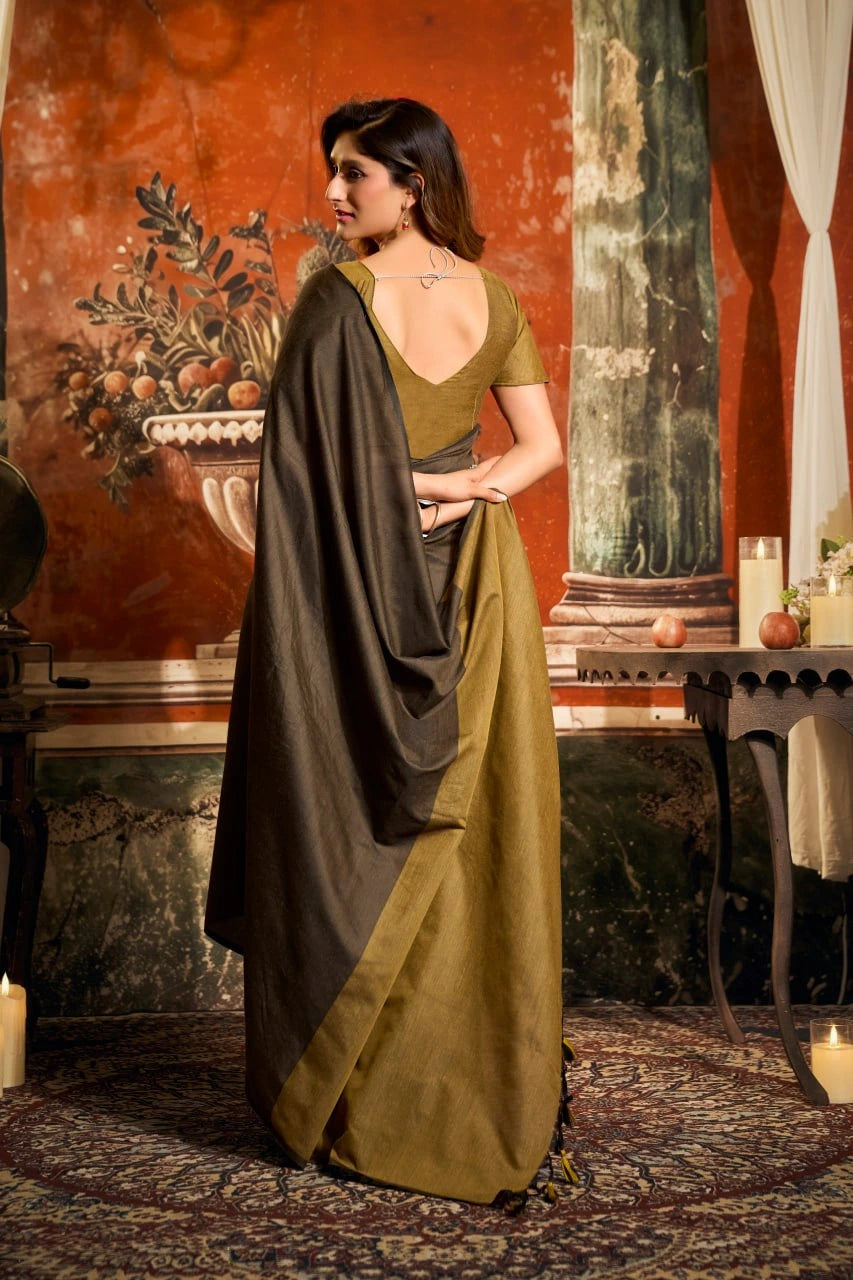 Woman in a green and gray saree standing in an ornate room with classical decor.