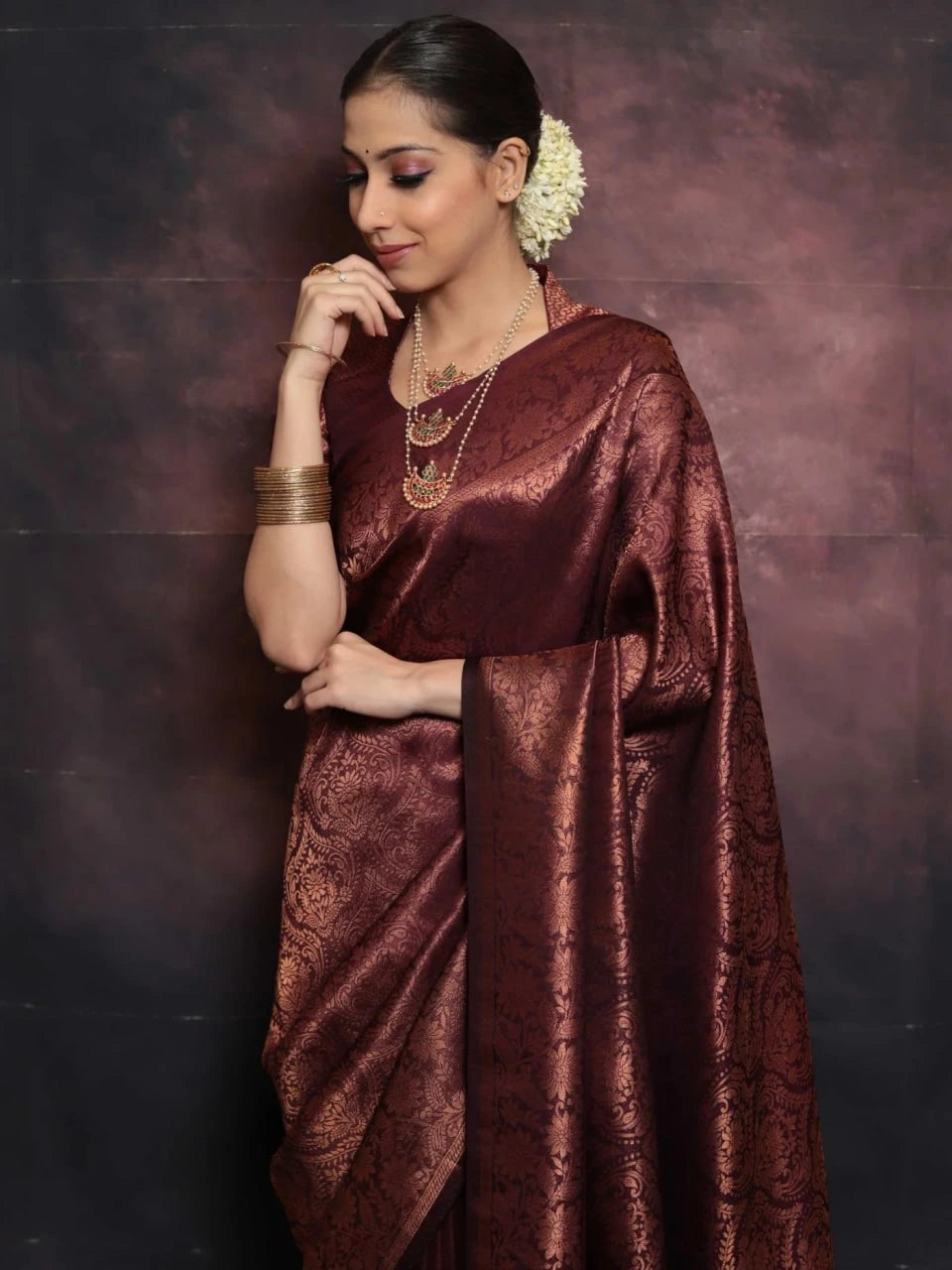 Woman wearing a maroon saree with a gold border against a dark background