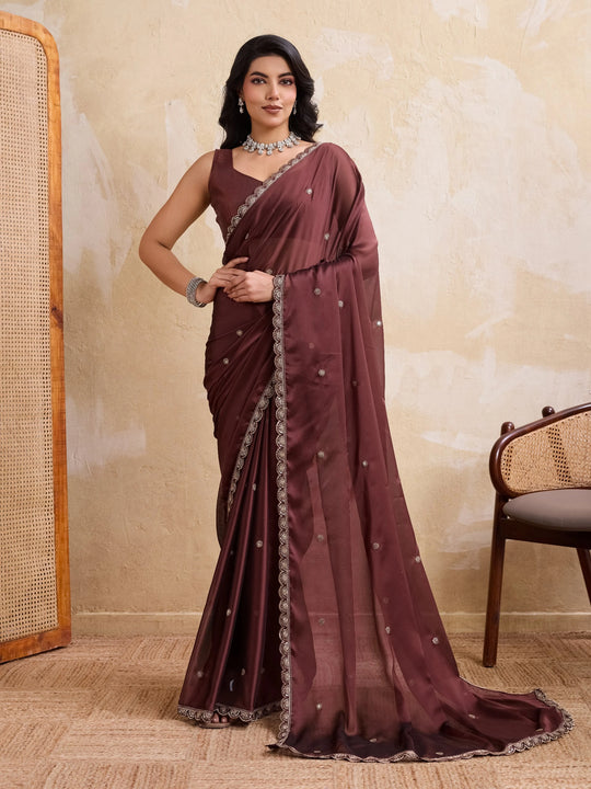 Woman wearing a maroon saree with a beige wall and chair in the background