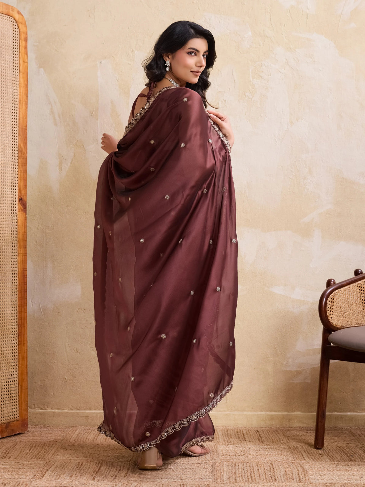 Woman in a maroon saree with white embellishments standing against a beige wall.