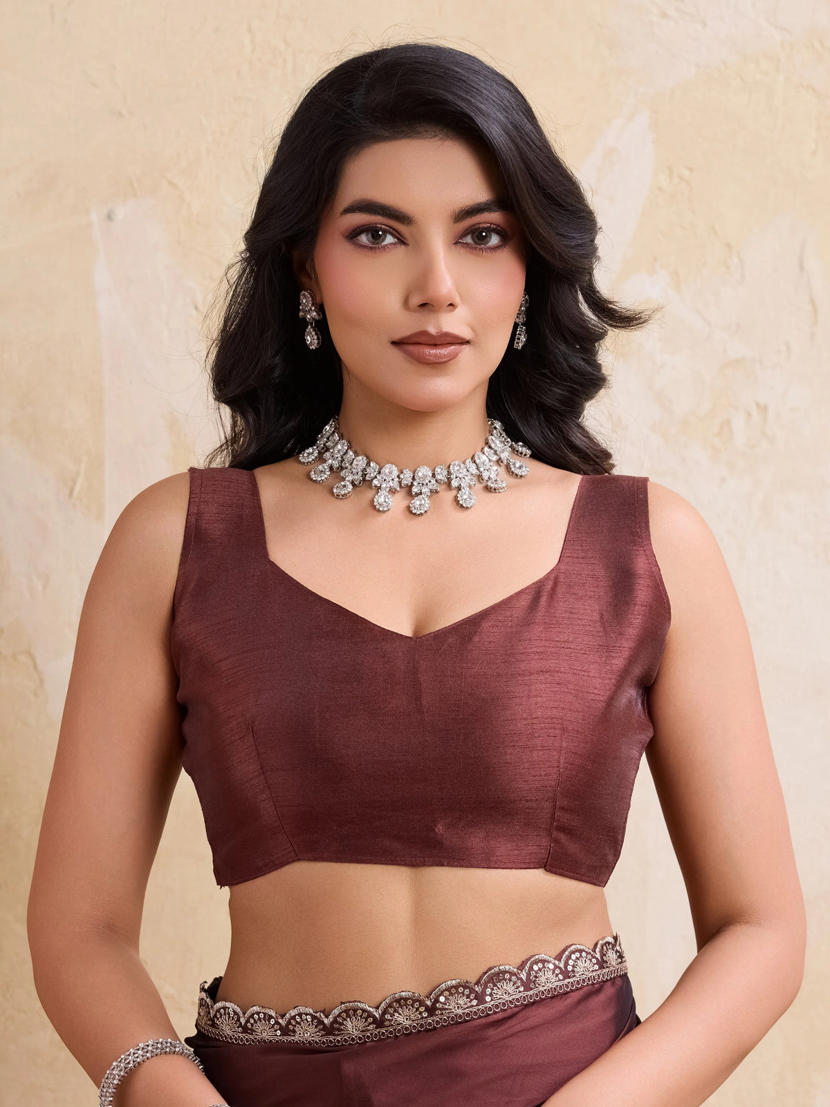 Woman wearing a brown saree with silver jewelry against a beige background