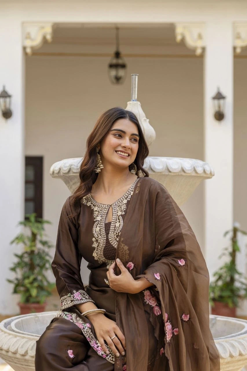 Woman in traditional brown outfit with floral details sitting outdoors.