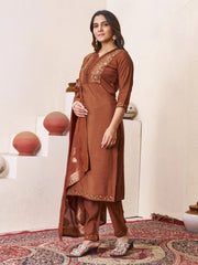 Woman wearing a brown traditional outfit with intricate designs in a room with decorative elements.