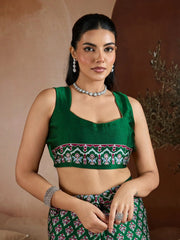 Woman wearing a green embroidered blouse with a patterned skirt against a brown background