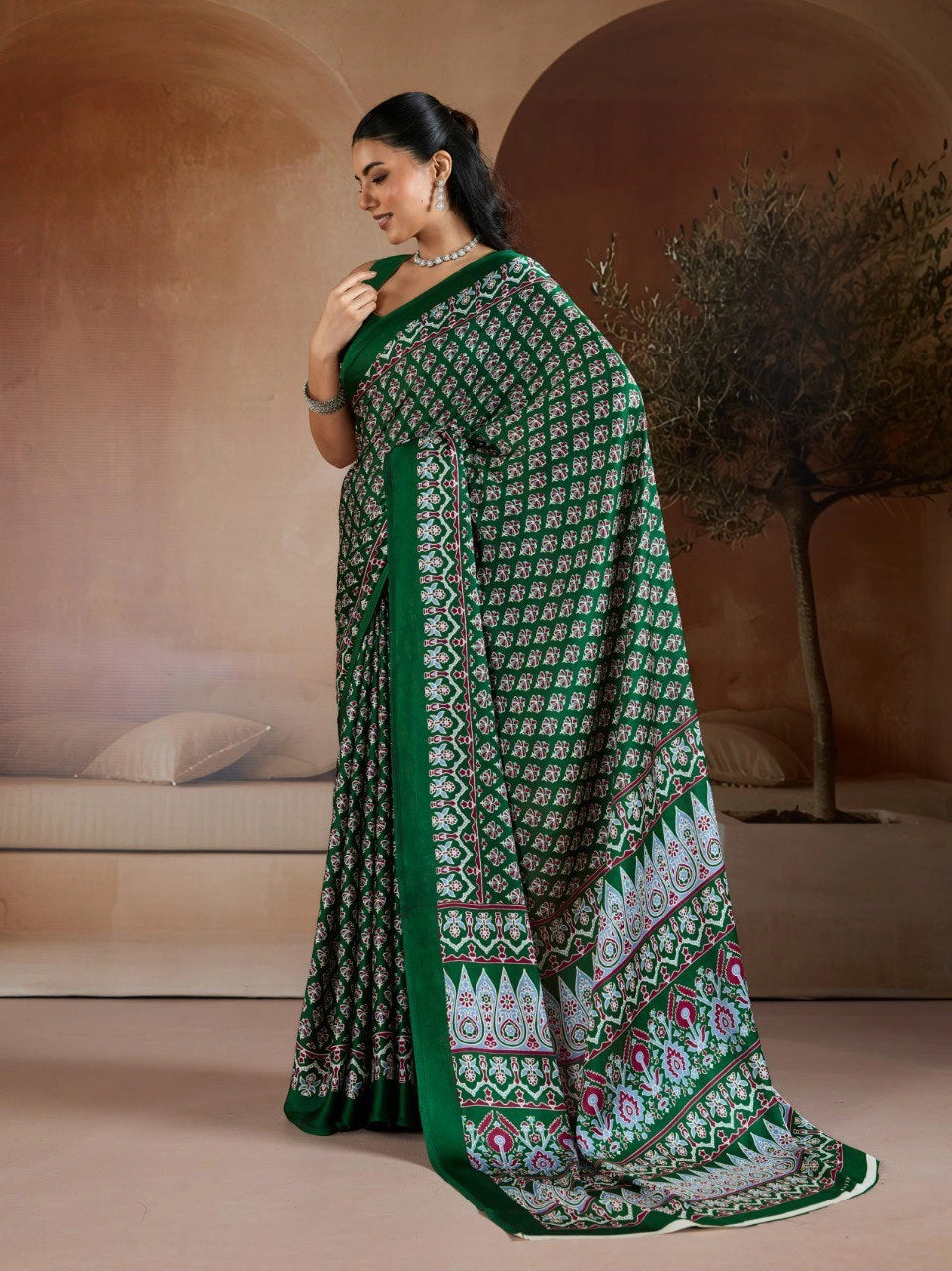 Woman wearing a green and patterned saree in an indoor setting with a neutral background