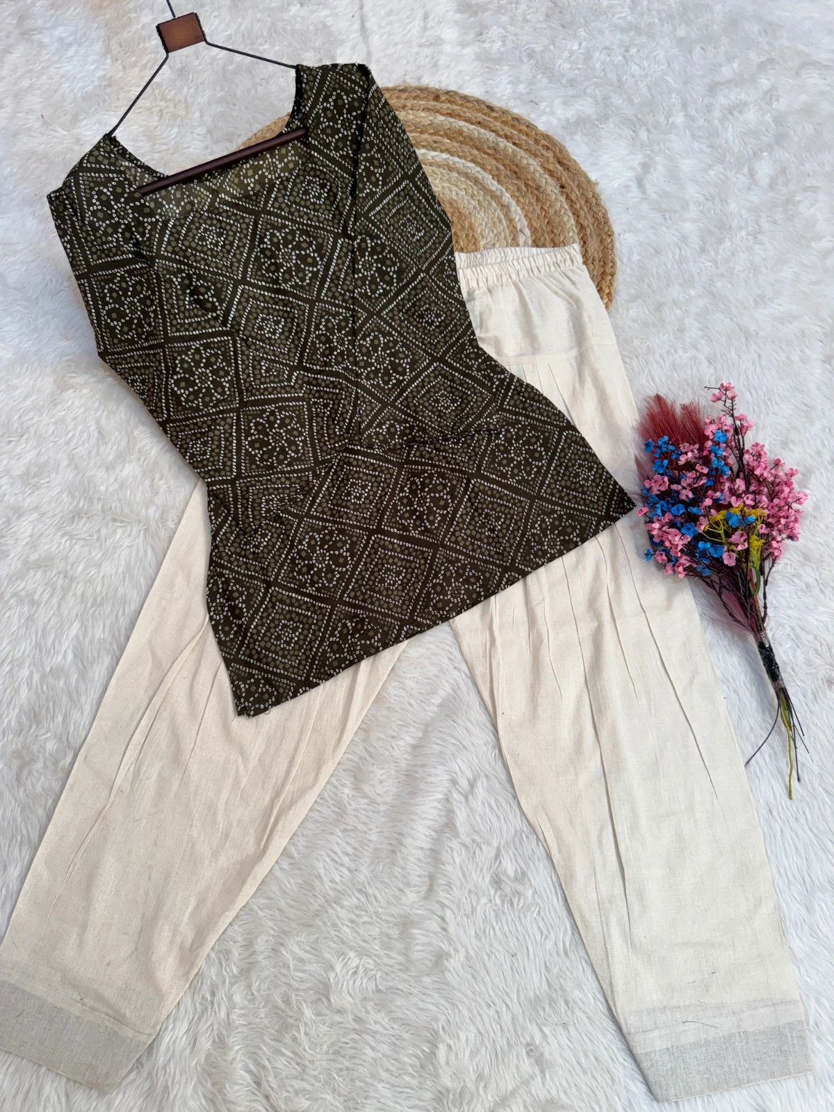 Black patterned top and beige pants on a white background with a small bouquet of flowers.