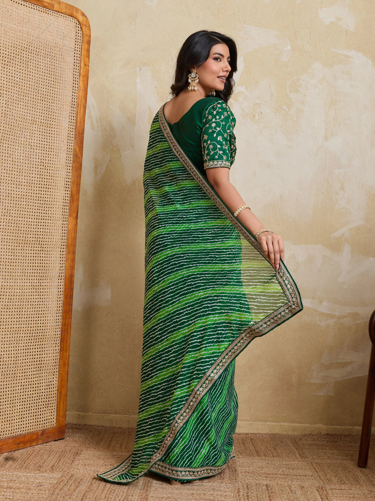 Woman wearing a green saree with a textured wall background
