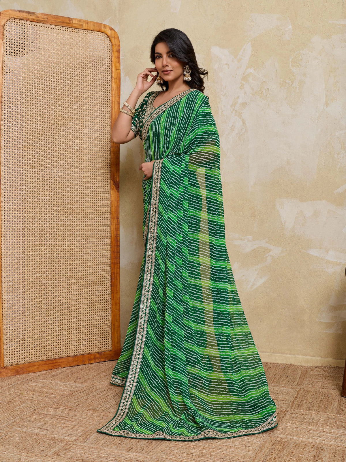 Woman wearing a green saree with a pattern against a beige wall.