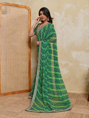 Woman wearing a green saree with a pattern against a beige wall.