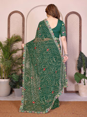 Woman wearing a green saree with intricate patterns in a decorative setting with plants.