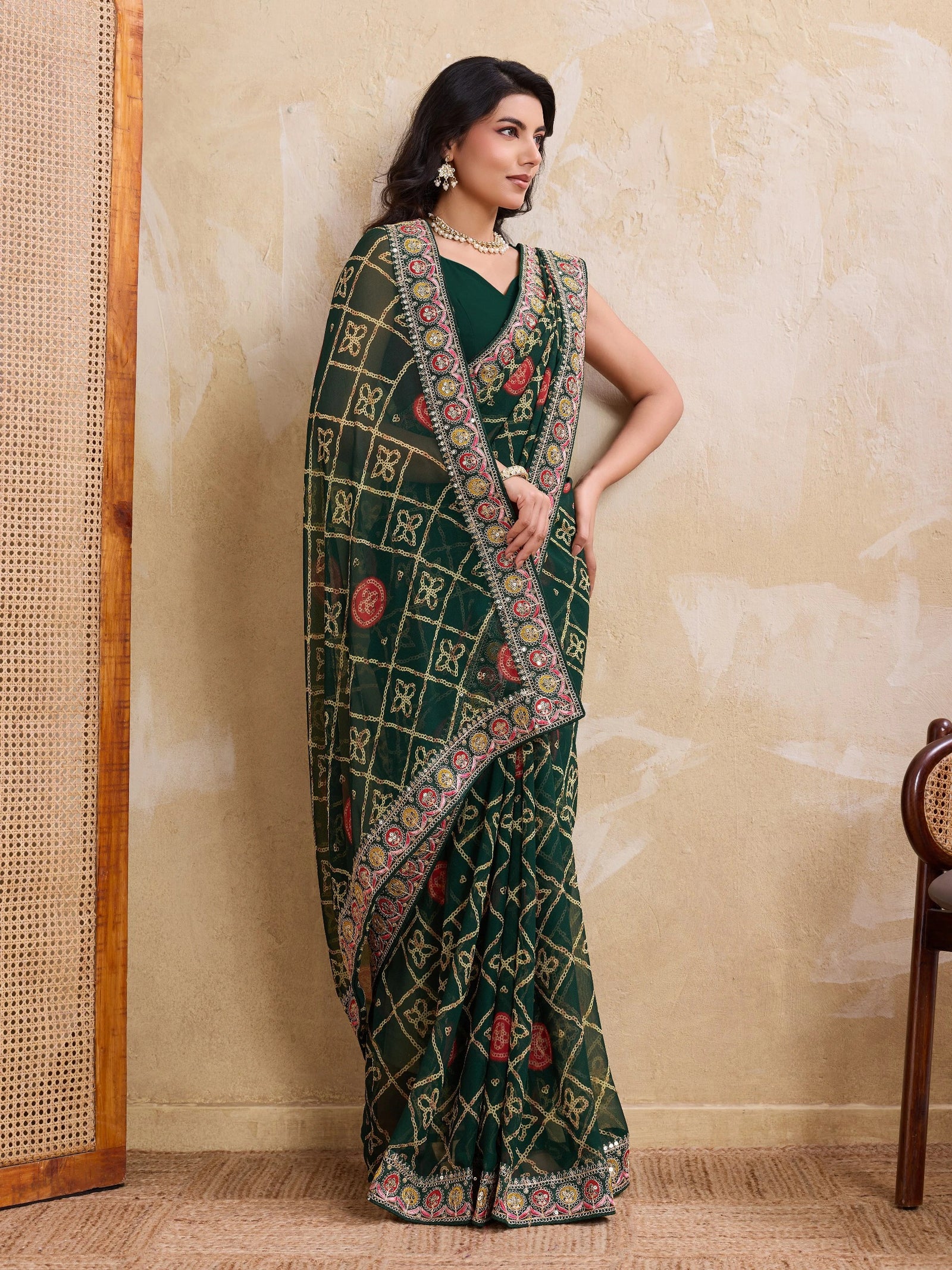Woman wearing a green saree with a patterned border against a beige wall.
