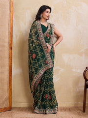 Woman wearing a green saree with a patterned border against a beige wall.
