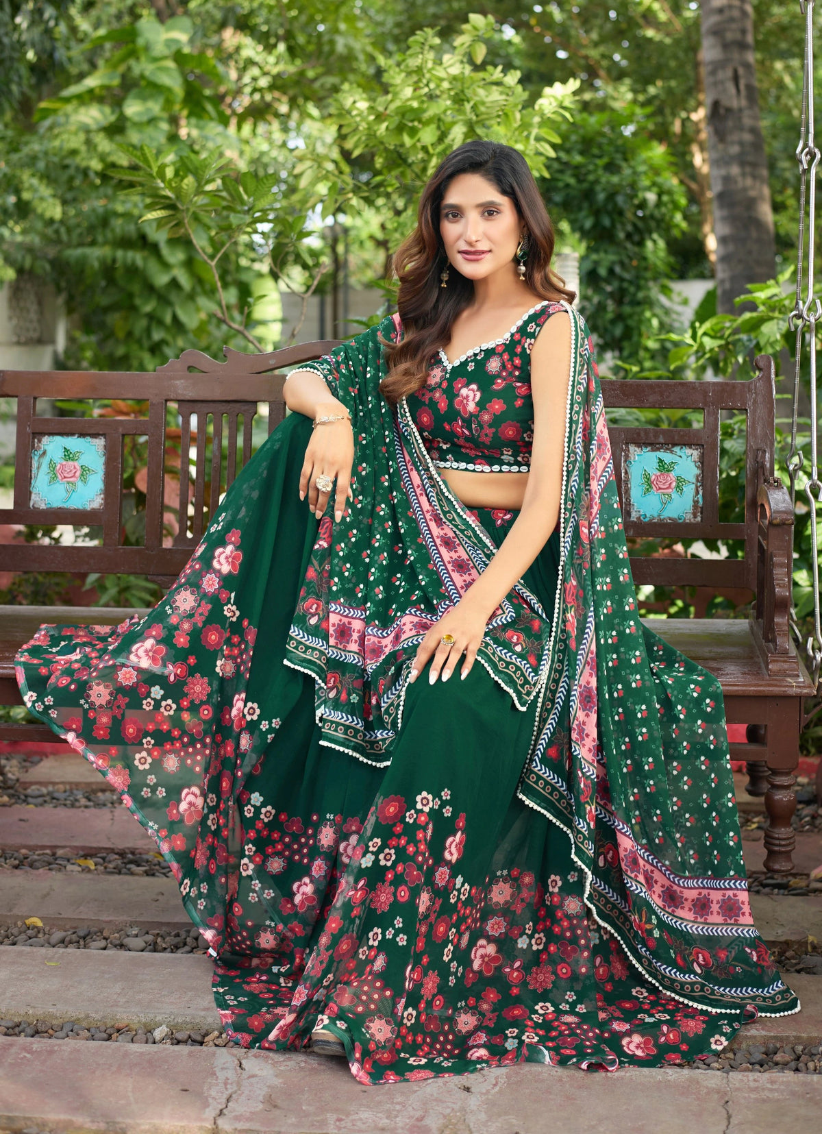 Woman in a green floral saree sitting on a swing with trees in the background