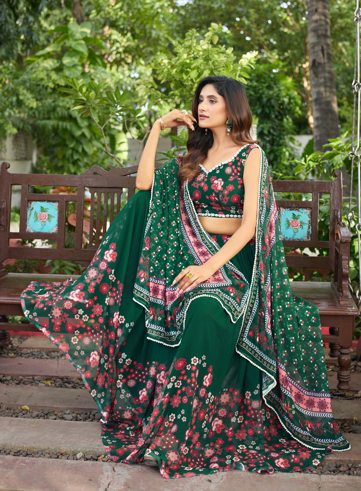 Woman in a green floral traditional outfit sitting on a bench outdoors.
