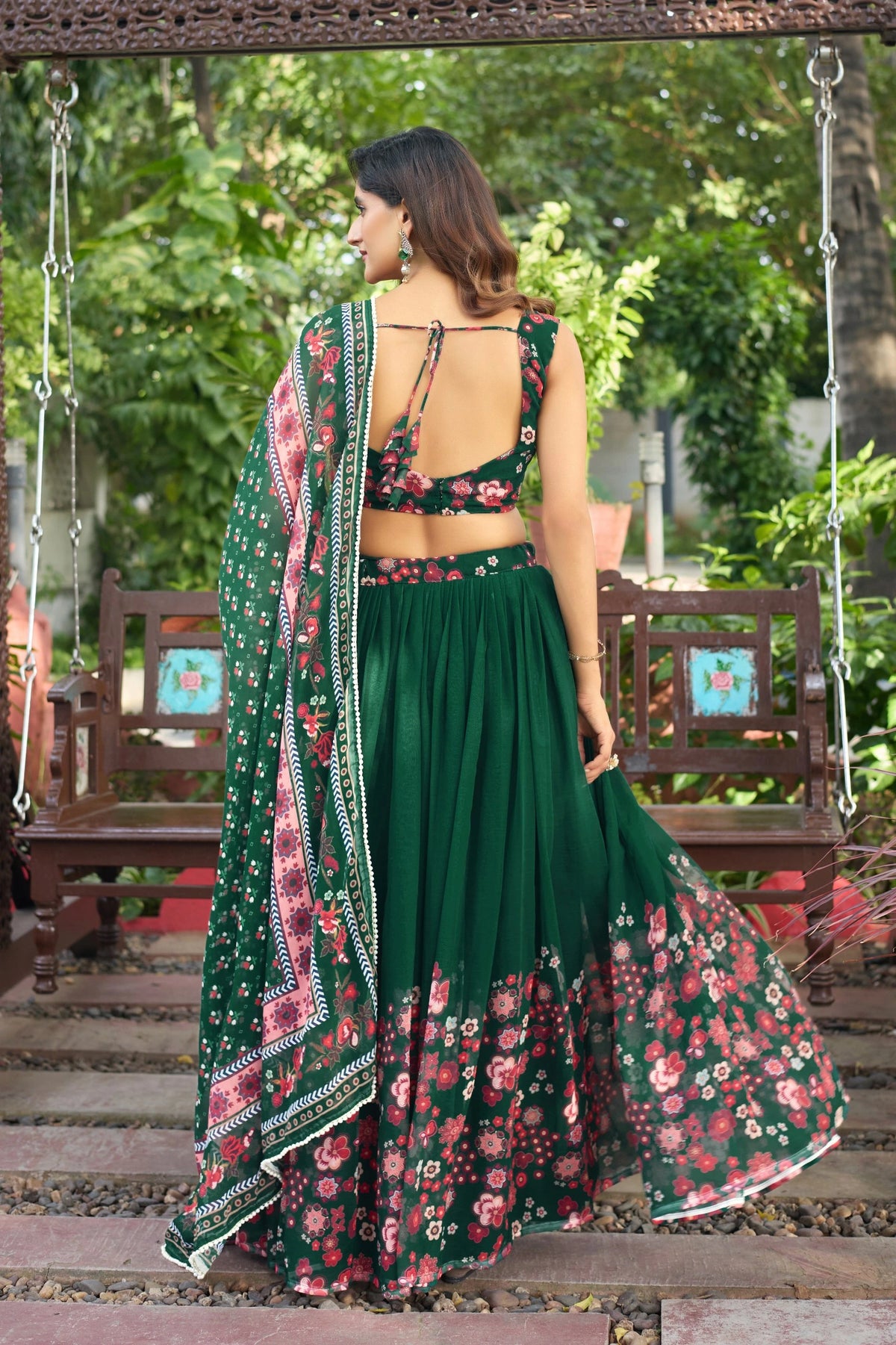 Woman in a green floral saree standing on a wooden platform with greenery in the background