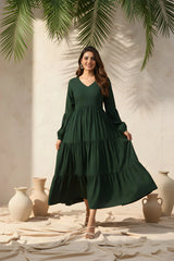 Woman wearing a green dress standing in a sunlit room with decorative vases and plants.