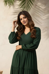 Woman wearing a green dress against a beige wall with leaf shadows