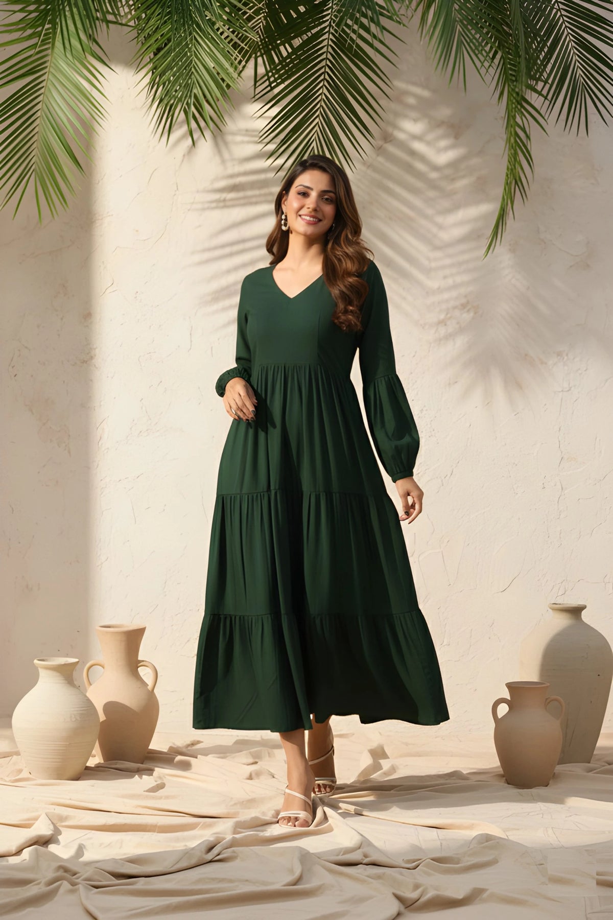 Woman in a green dress standing in front of a neutral wall with decorative vases and plants.