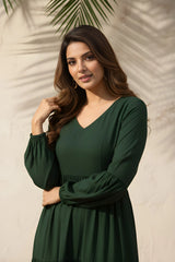 Woman wearing a green dress standing against a neutral background with a palm leaf.