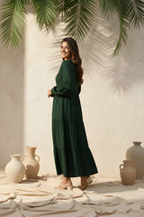 Woman in a green dress standing in a decorative setting with vases and palm leaves.
