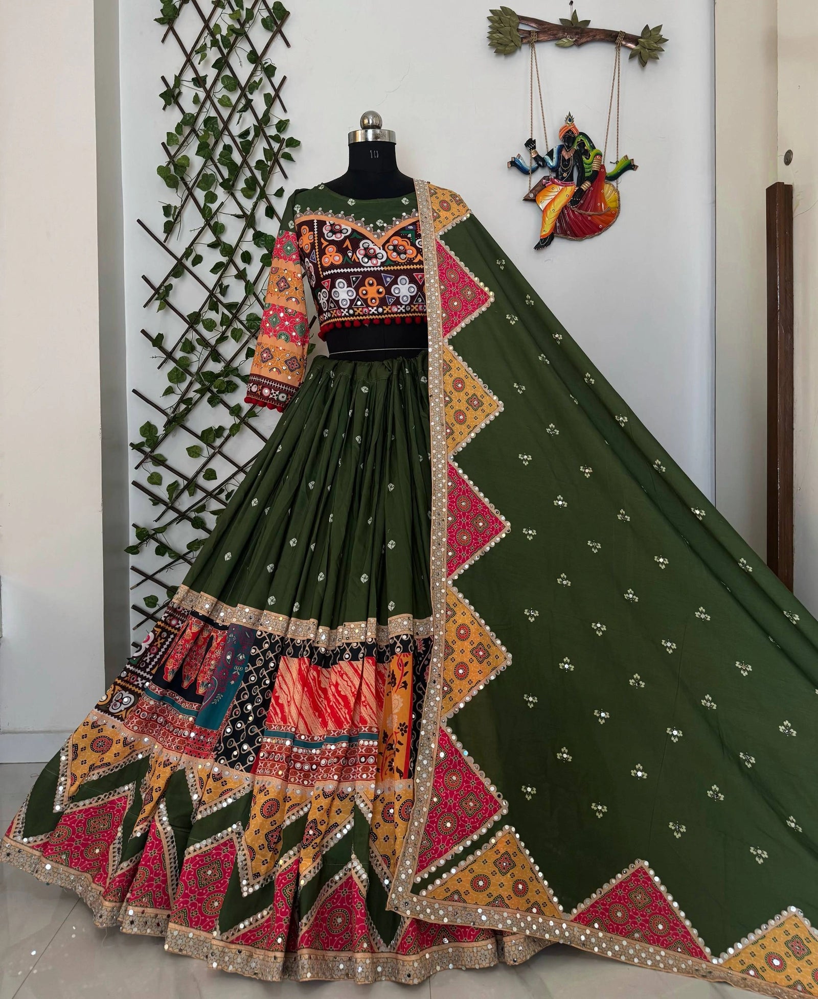 Traditional green embroidered outfit with colorful patterns on a mannequin against a white wall.