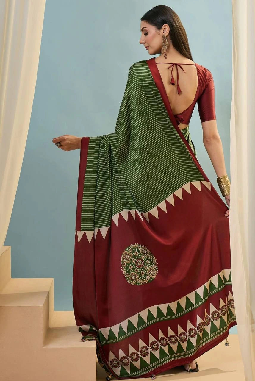 Woman wearing a traditional saree with a green and red pattern, standing against a light blue wall.