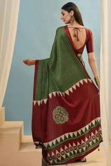 Woman wearing a traditional saree with a green and red pattern, standing against a light blue wall.