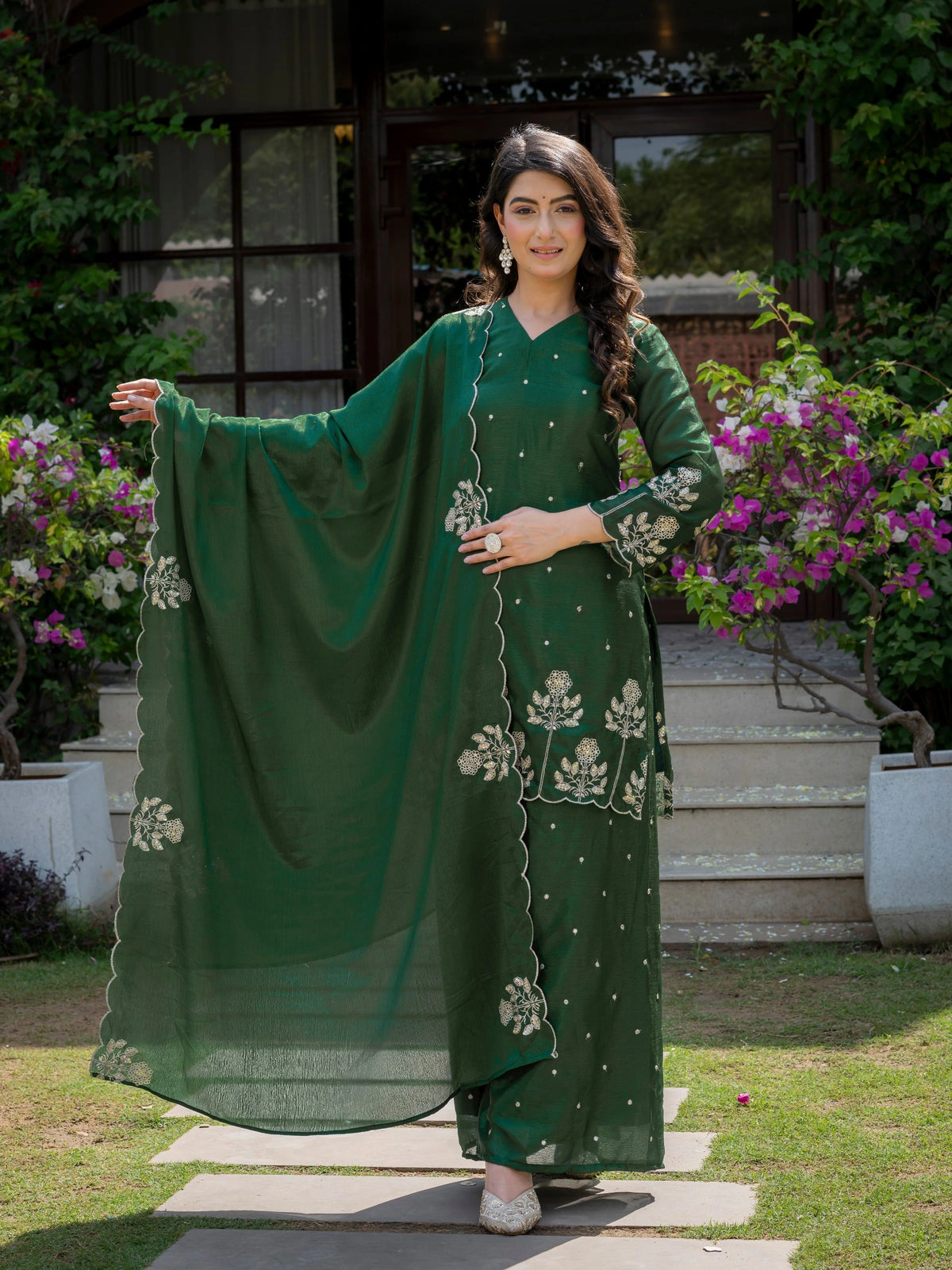 Woman in a green traditional outfit with floral patterns standing outdoors.