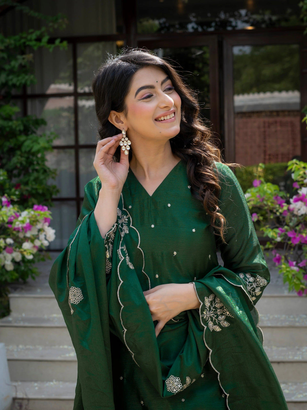 Woman in a green traditional outfit with floral earrings, standing outdoors.
