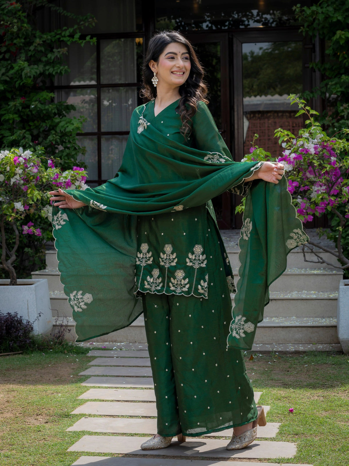 Woman in a green traditional outfit with floral patterns standing outdoors.