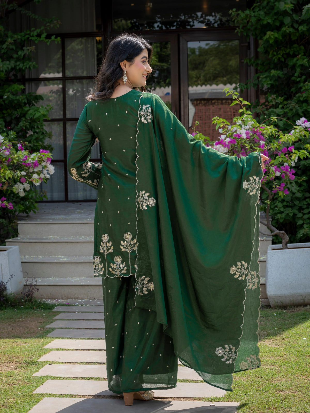 Woman in a green traditional outfit with floral patterns standing outdoors.