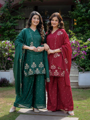 Two women in traditional green and red outfits standing outdoors with a garden background.