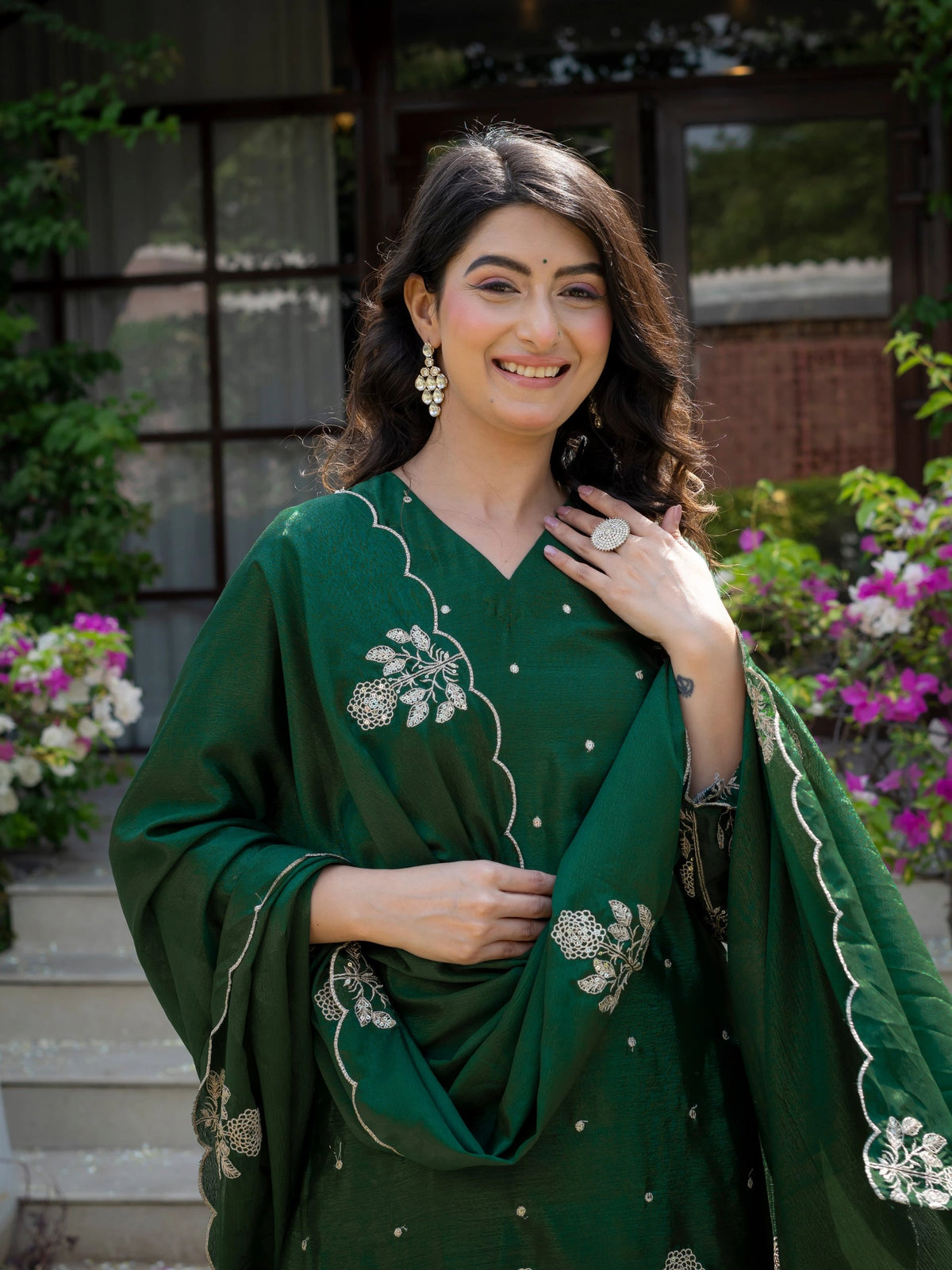 Woman in a green traditional outfit with floral patterns standing outdoors.