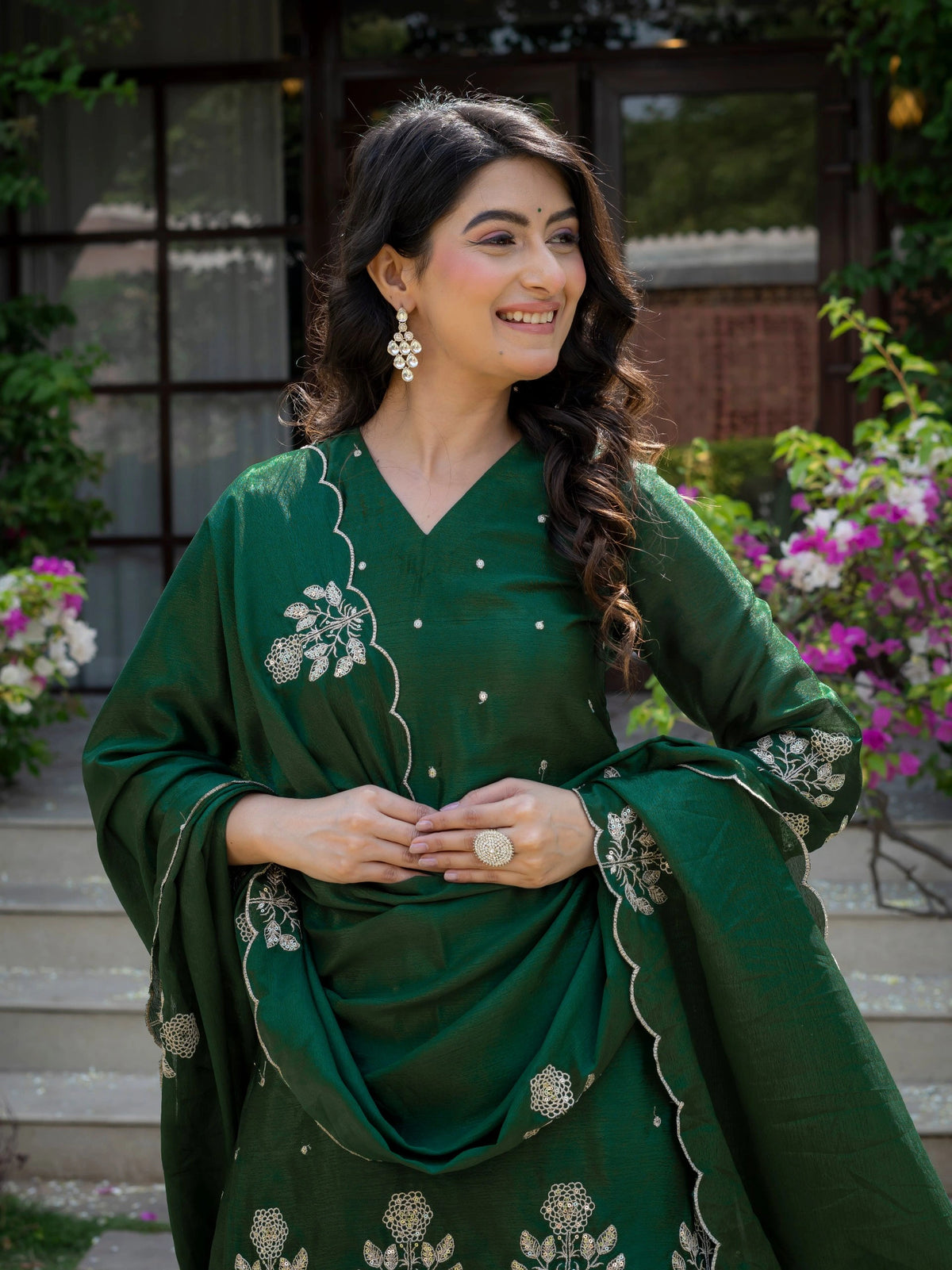 Woman in a green traditional outfit with floral embroidery standing outdoors.