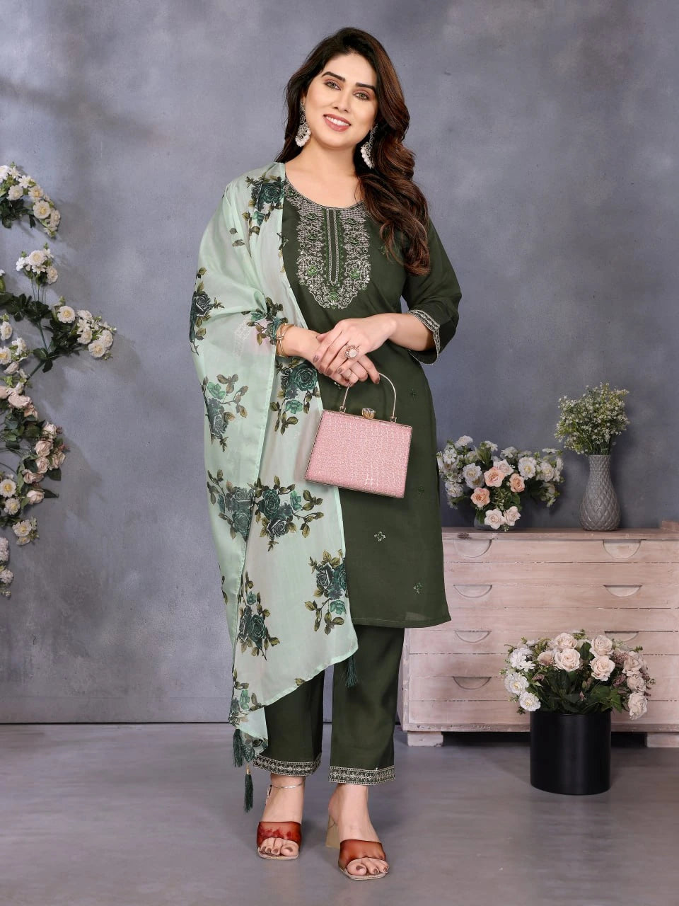 Woman in green traditional outfit with floral dupatta standing against a gray background with decorative elements.