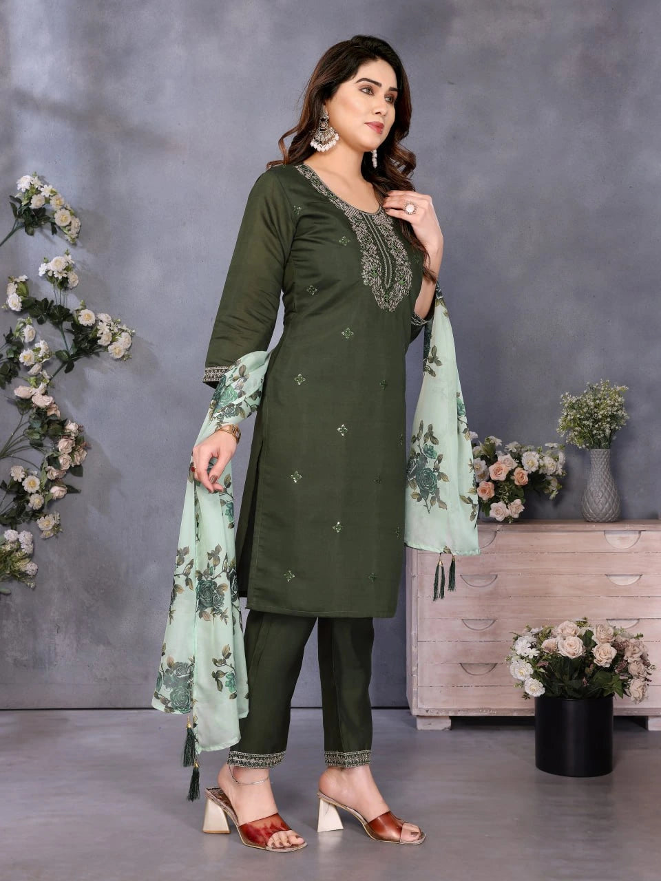 Woman in a green traditional outfit with a light green dupatta, standing against a gray background with decorative elements.