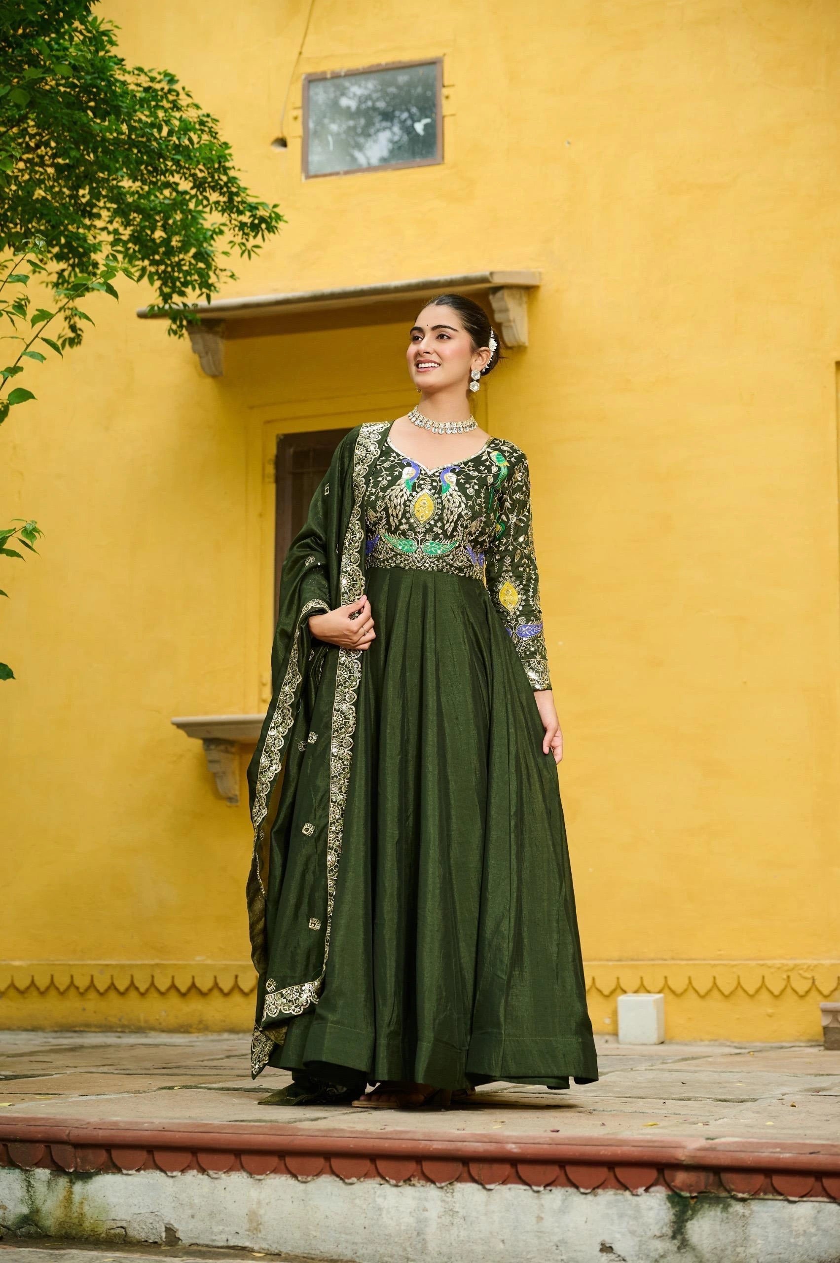 Woman in a green traditional outfit standing against a yellow wall.