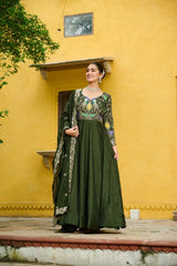 Woman in a green traditional outfit standing against a yellow wall.