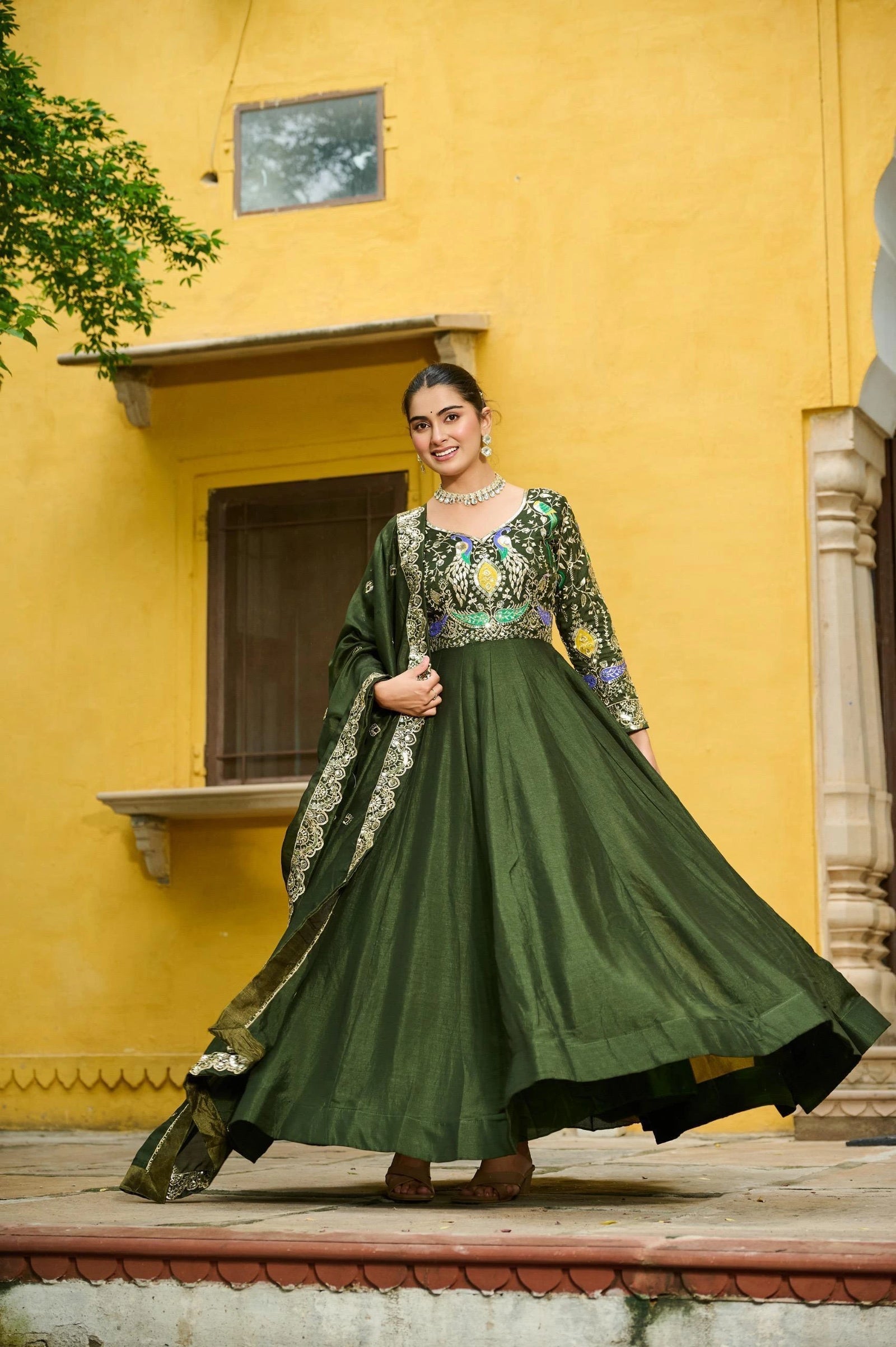 Woman in a green traditional outfit standing in front of a yellow building