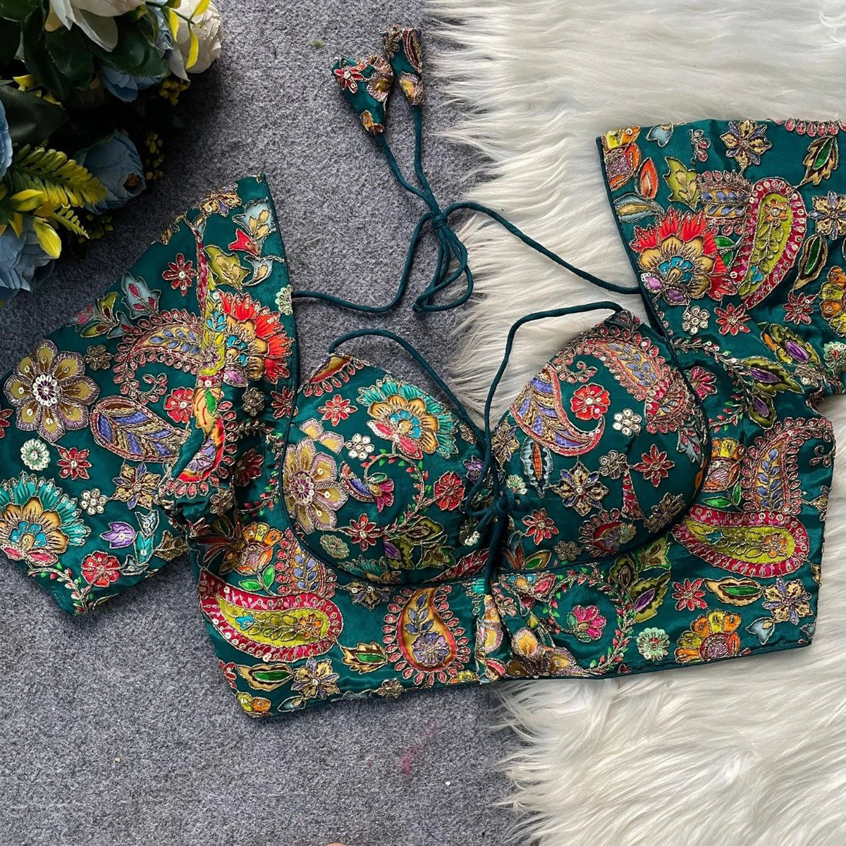 Colorful embroidered bikini set on a textured surface with flowers in the background