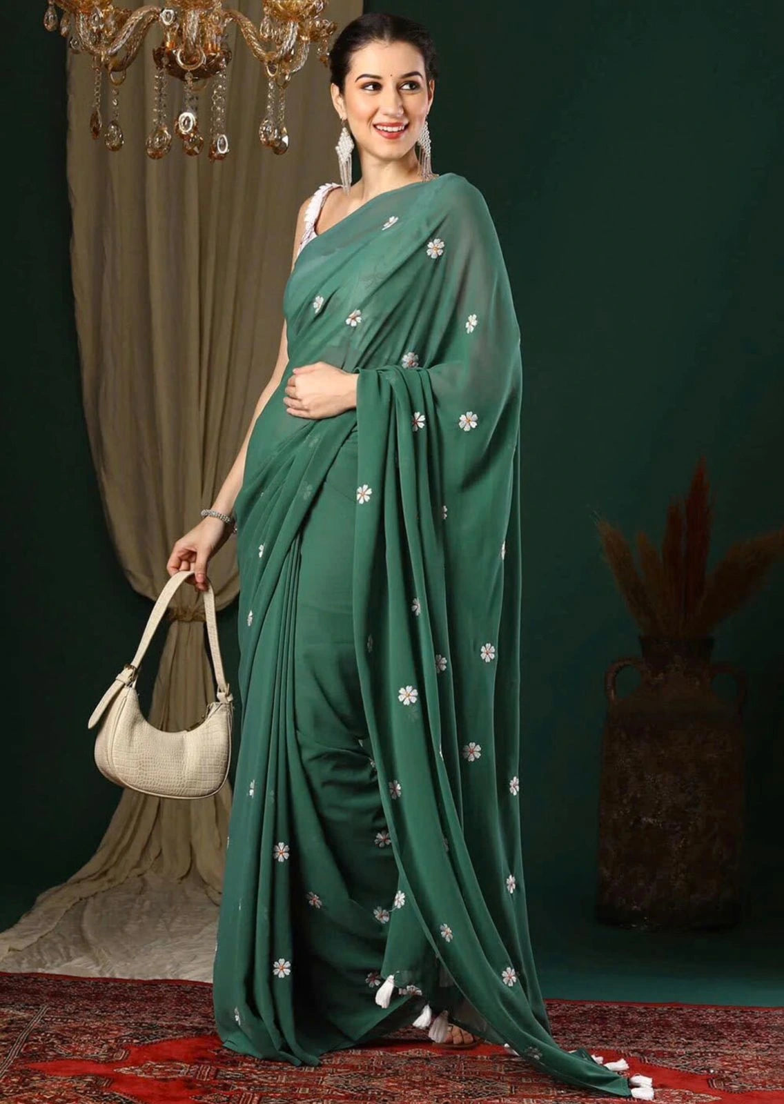 Woman in a green saree with white patterns holding a beige handbag against a dark background.