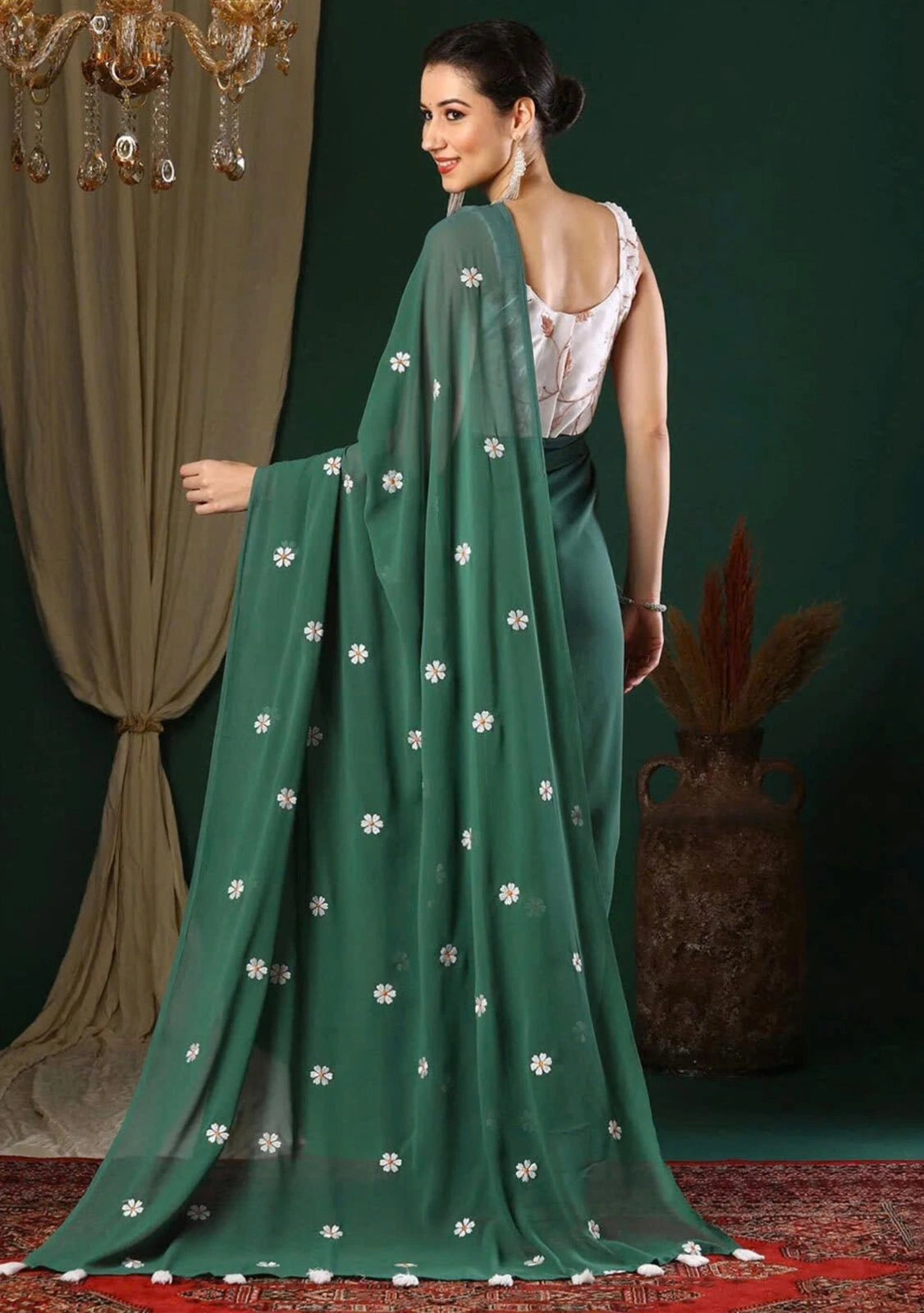 Woman wearing a green saree with white patterns in a decorated indoor setting