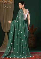 Woman wearing a green saree with white patterns in a decorated indoor setting