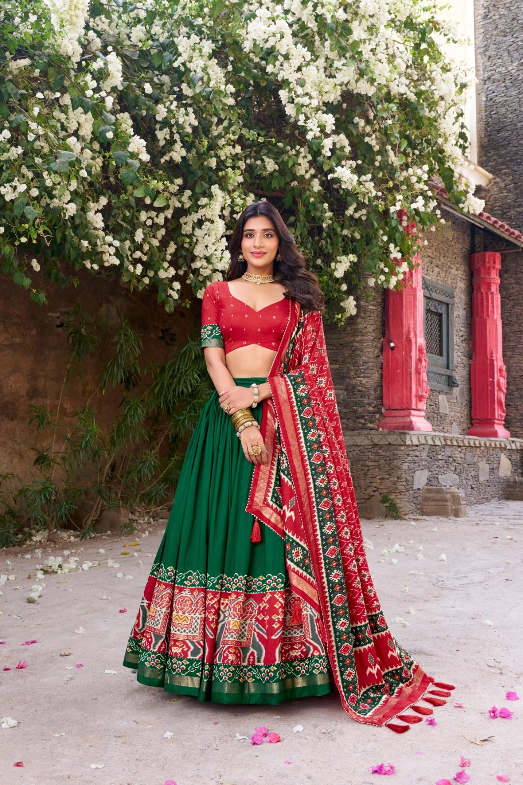 Woman in a red and green traditional outfit standing in front of a floral backdrop