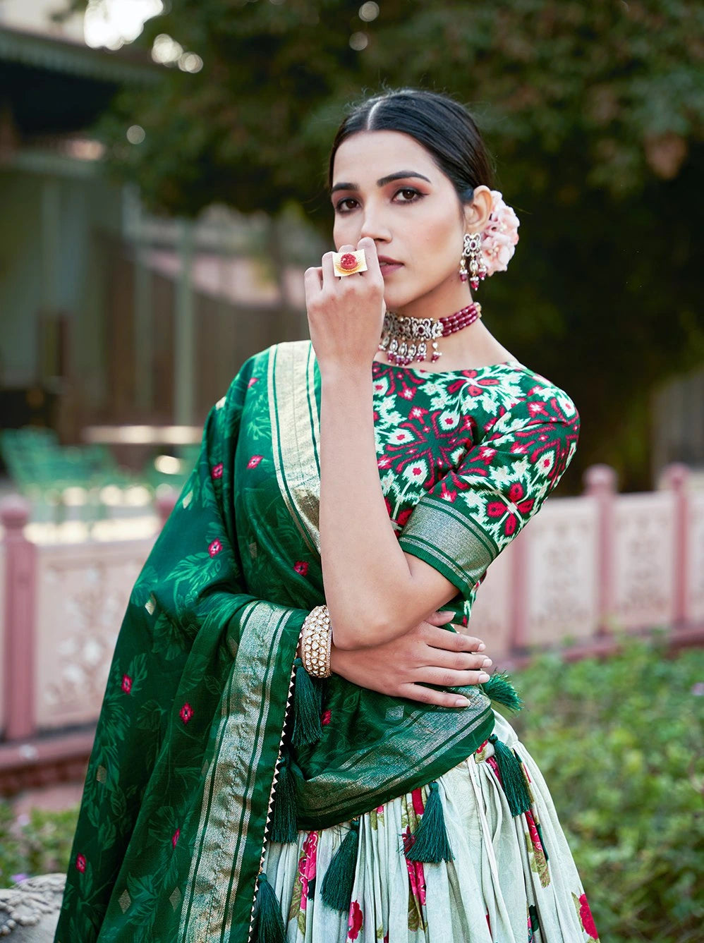 Woman in a green saree with floral patterns, standing outdoors.