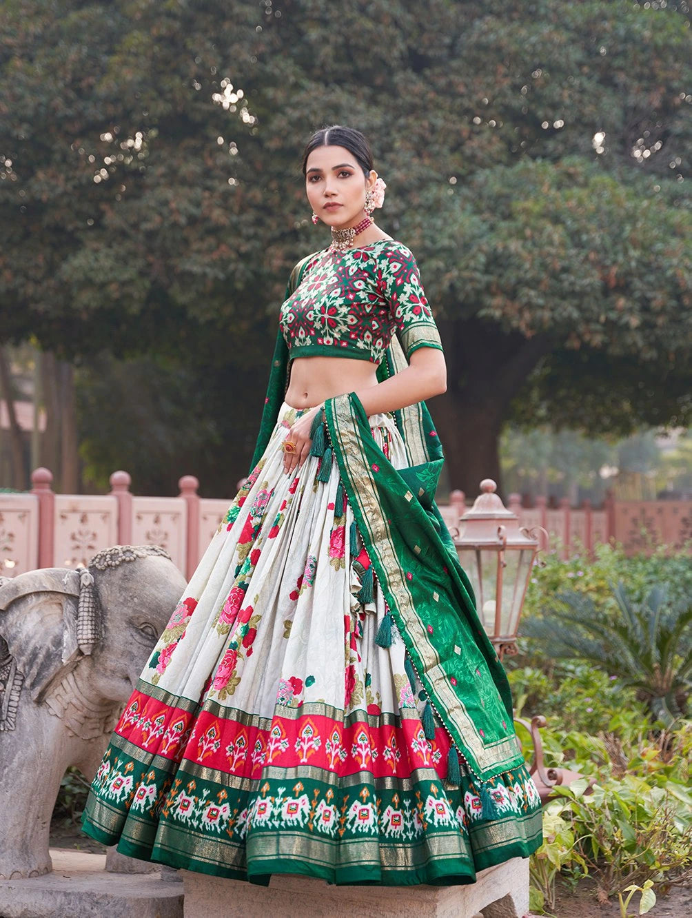 Woman in a traditional floral outfit standing outdoors with greenery in the background