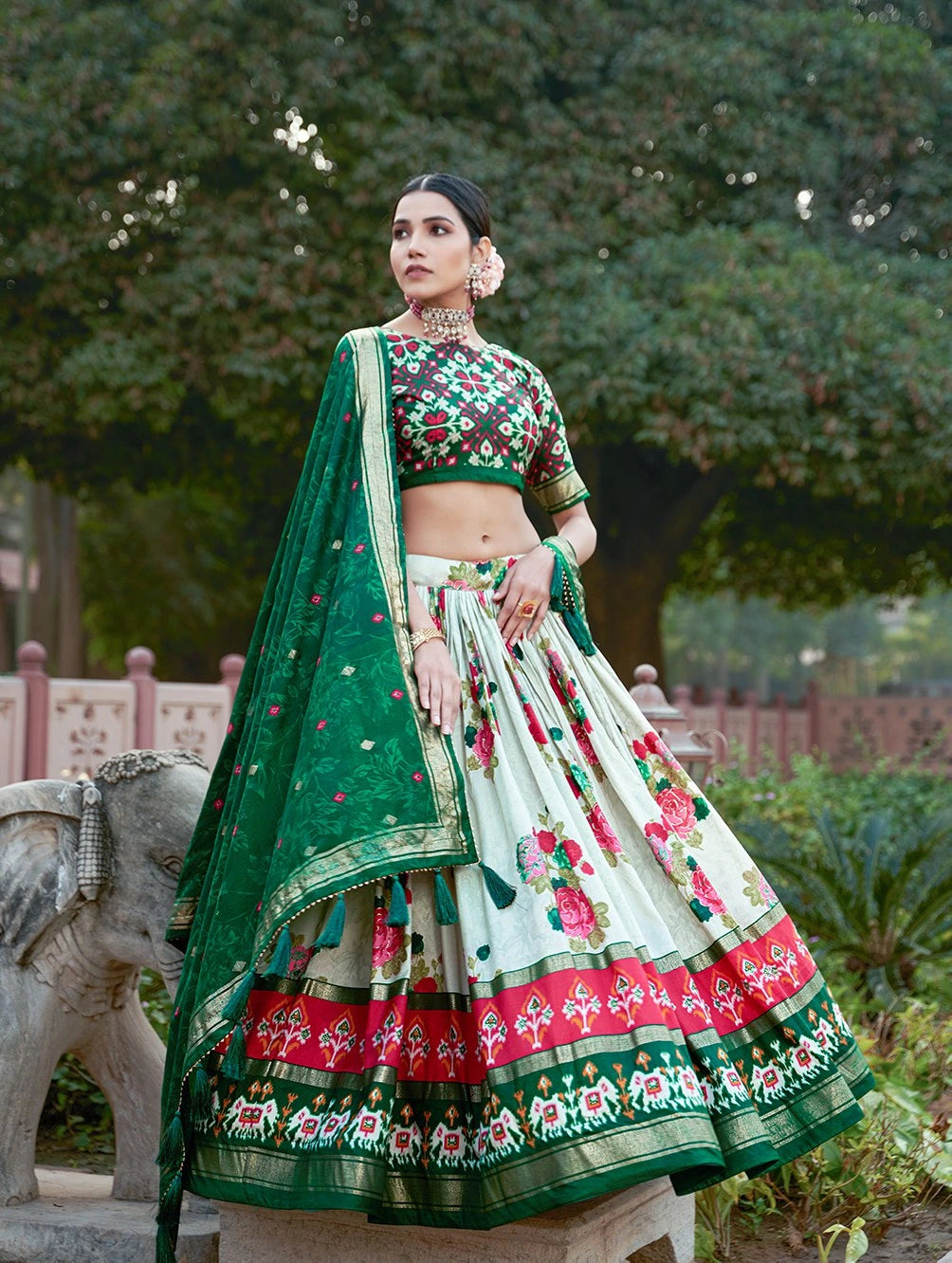 Woman in a traditional green and white embroidered outfit standing outdoors with trees in the background